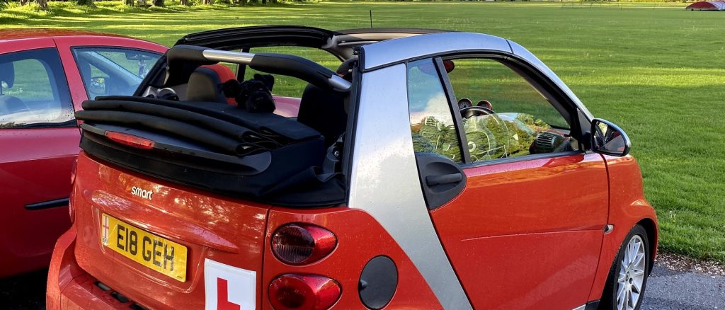 Red car with a learner driver 'L' plate, parked in a park.